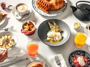 A breakfast setting with various dishes, a teapot, and a glass of orange juice.