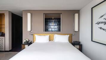 Una habitación de hotel con una cama grande, un cabecero, dos mesitas de noche, una lámpara de noche, un adorno en la pared y una obra de arte enmarcada.