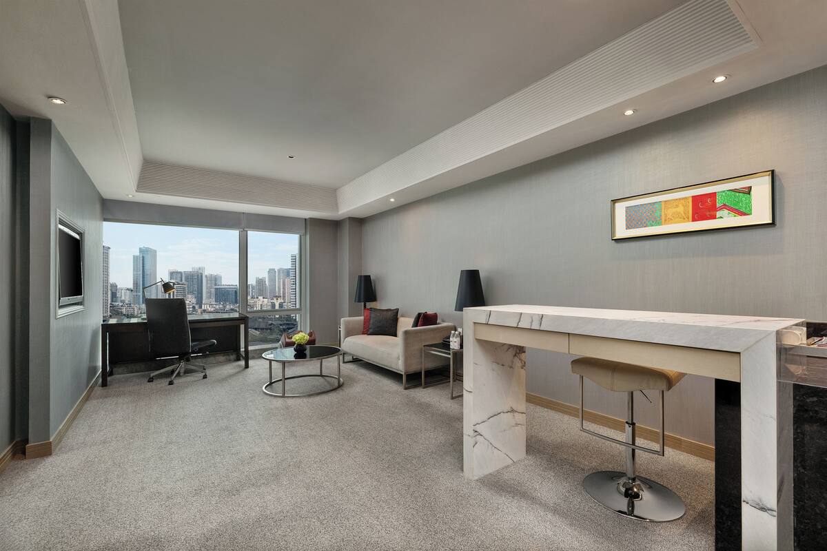 Une chambre d’hôtel moderne avec vue sur la ville, un bureau, un canapé et un coin bar.