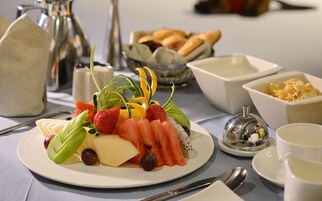 Un desayuno con una fuente de fruta, pan y una taza de café.