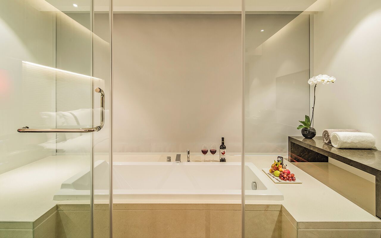 Un baño moderno con ducha de vidrio, una bañera grande y un tocador con espejo y una orquídea en maceta.
