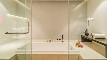 Un baño moderno con ducha de vidrio, una bañera grande y un tocador con espejo y una orquídea en maceta.