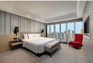 Una habitación de hotel moderna con una cama grande, un sillón rojo y vistas a la ciudad.