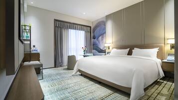 A modern hotel room with a large bed, a desk, a chair, and a large window with curtains.