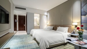 Una habitación de hotel moderna con una cama grande, mesitas de noche, un televisor de pantalla plana y vistas al pasillo.