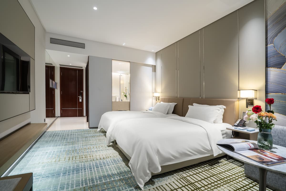 Una habitación de hotel moderna con una cama grande, mesitas de noche, un televisor de pantalla plana y vistas al pasillo.