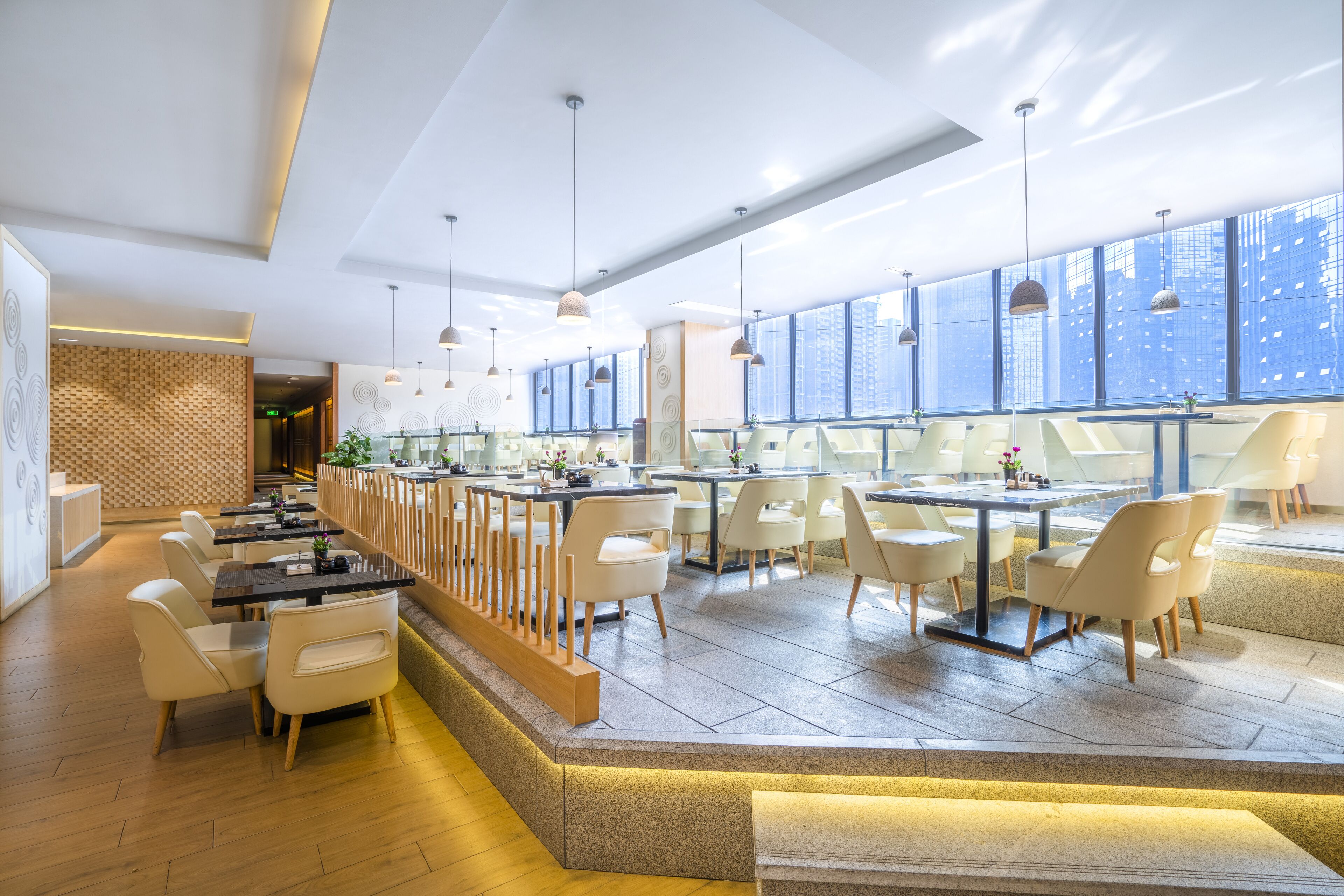 Ein modernes Restaurant mit einer langen Theke, weißen Stühlen und Pendelleuchten.