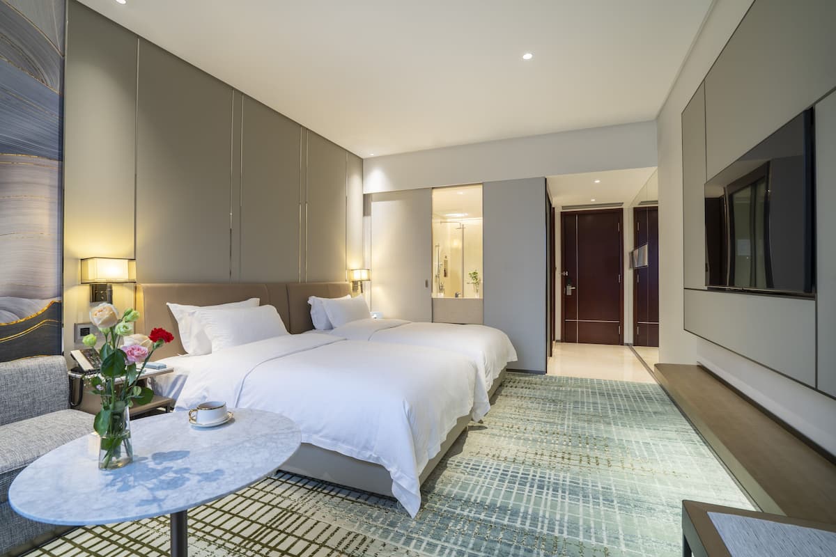 Una habitación de hotel moderna con una cama grande, un rincón de descanso con una mesa y sillas, y un televisor montado en la pared.