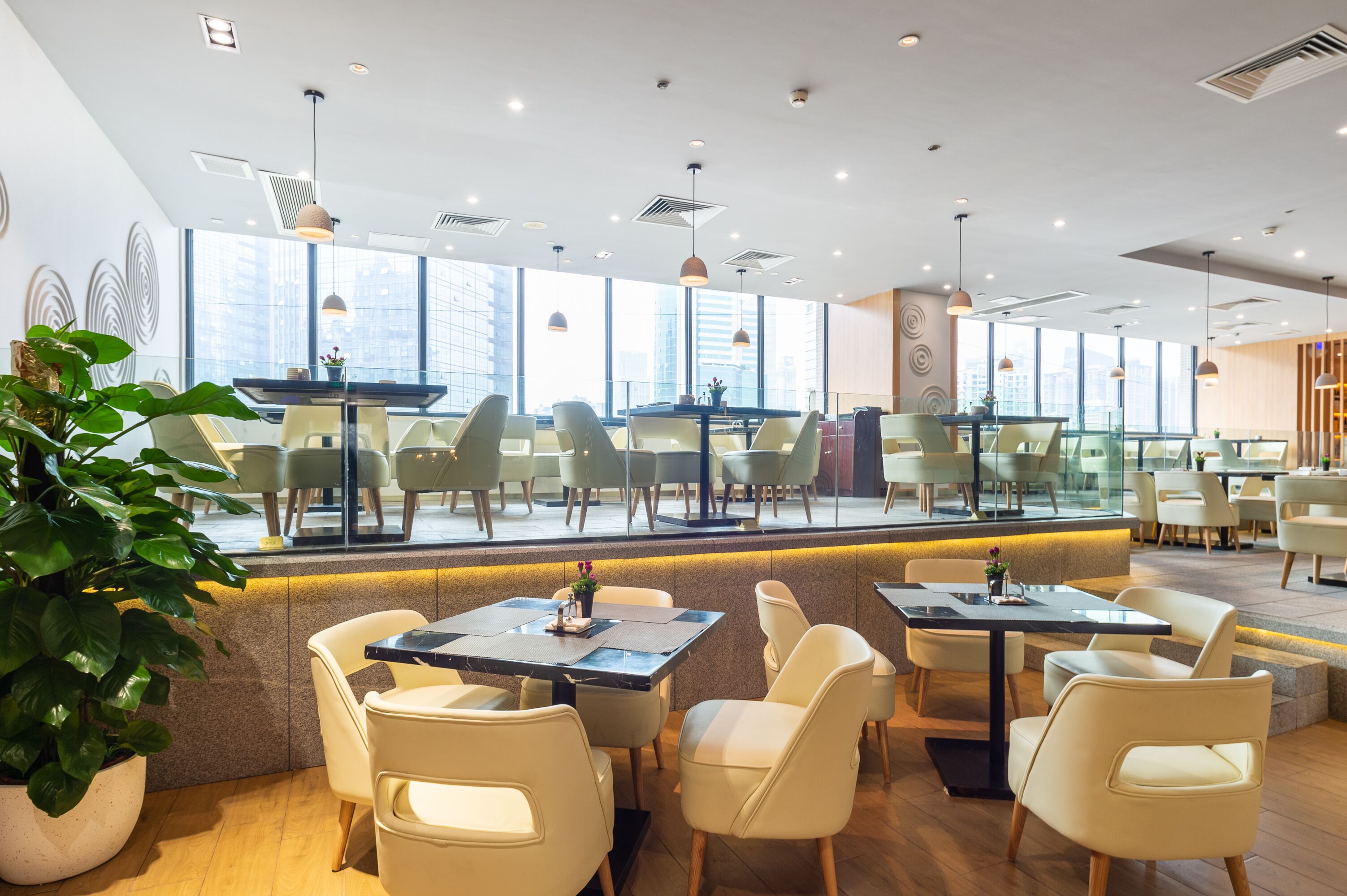 A modern restaurant with a glass partition, wooden flooring, and a view of the cityscape.
