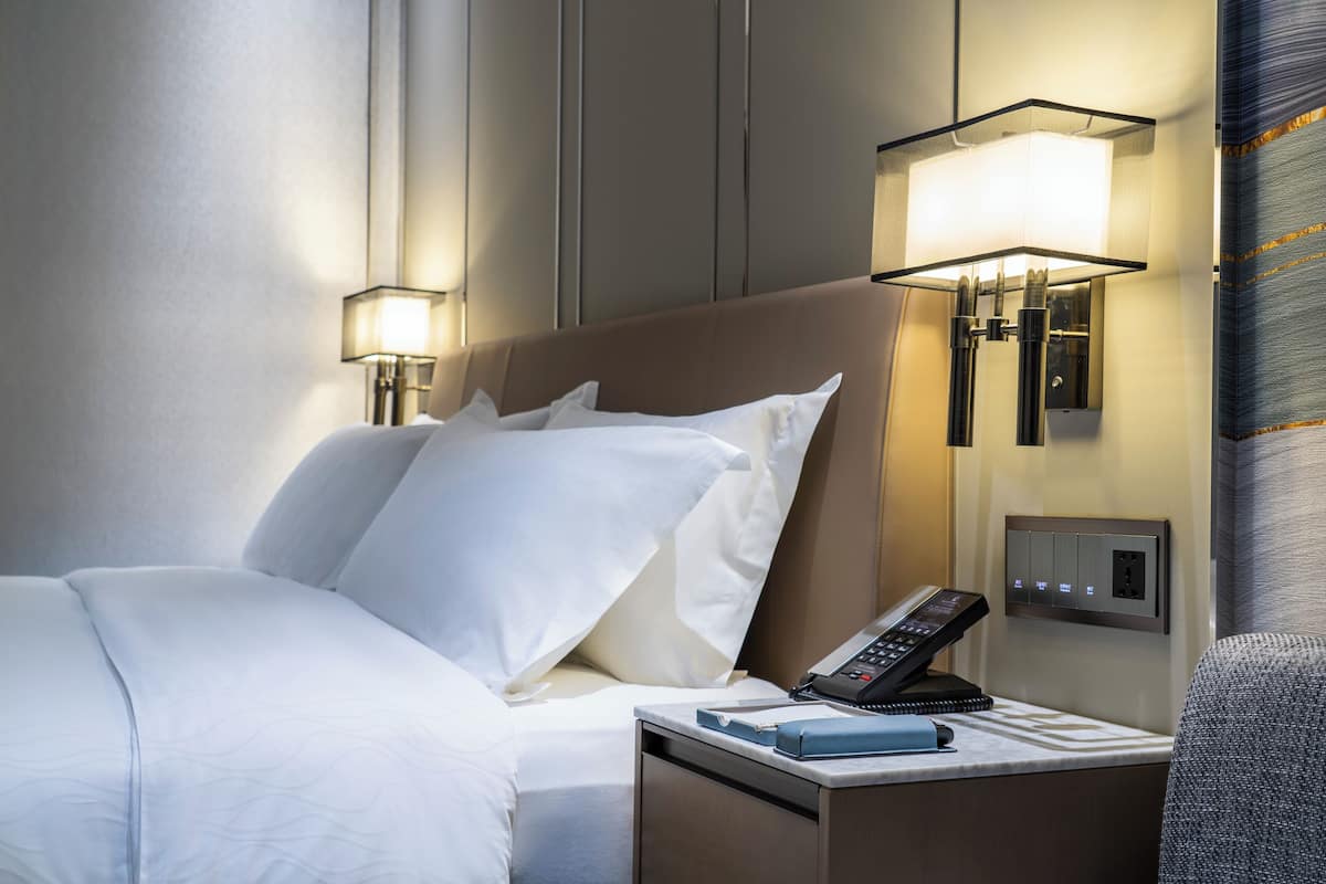 Habitación de hotel con una cama bien hecha, lámparas de noche, un teléfono y una mesita con un libro.