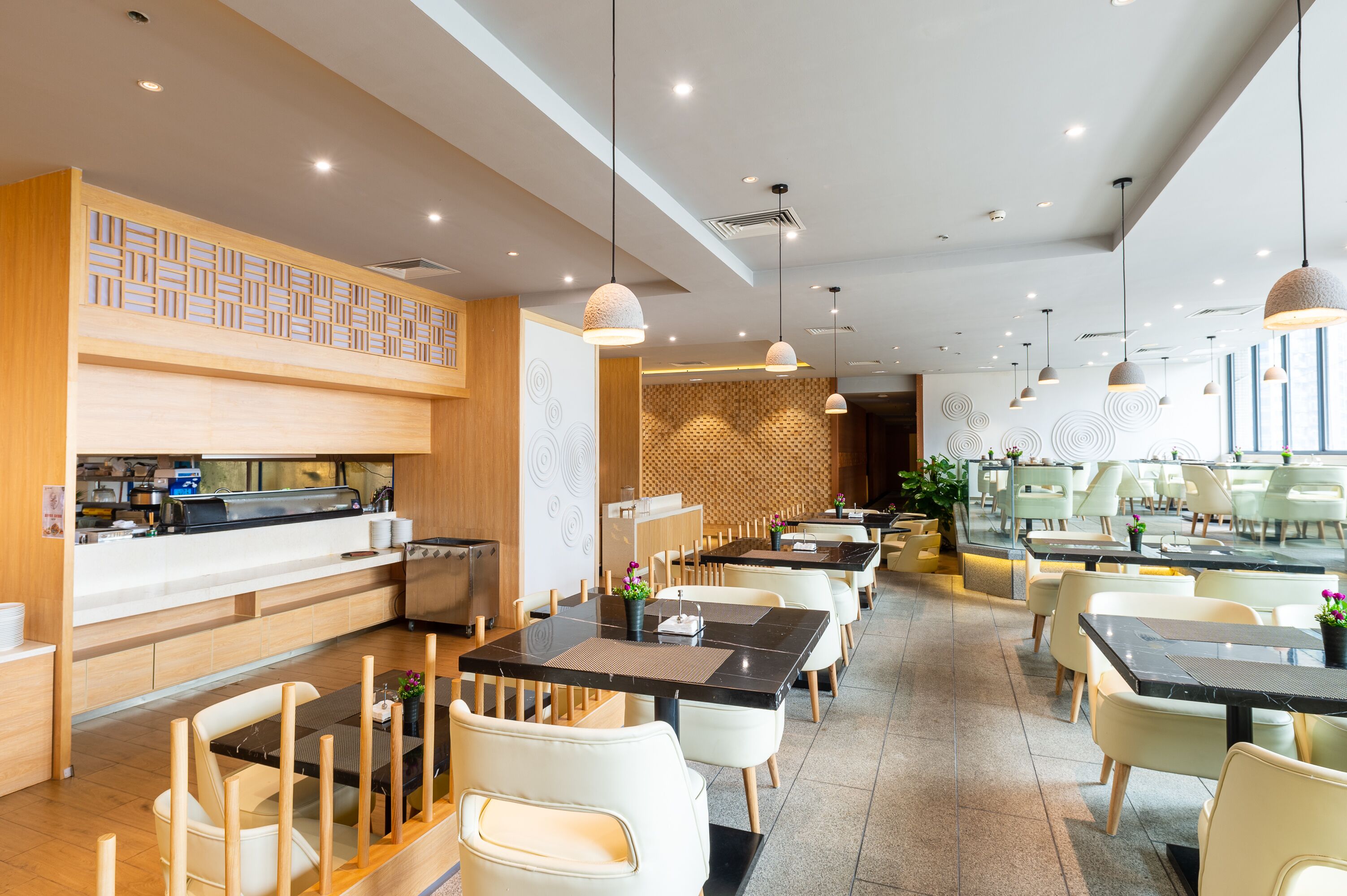 A modern restaurant with a long counter, multiple tables, and hanging pendant lights.