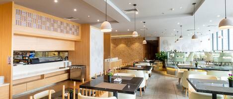 A modern restaurant with a long counter, multiple tables, and hanging pendant lights.