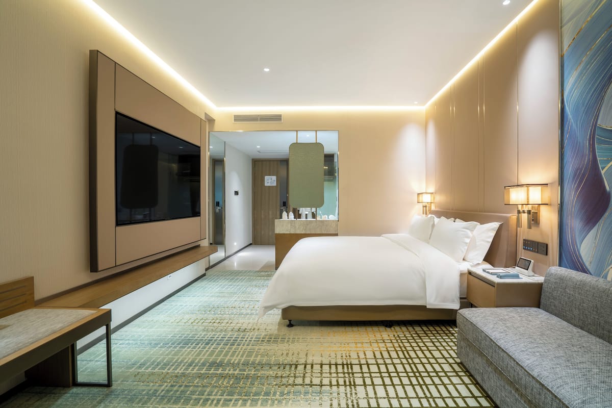 Una habitación de hotel moderna con una cama grande, un sofá, un televisor de pantalla plana, una mesita de noche y un espejo amplio.