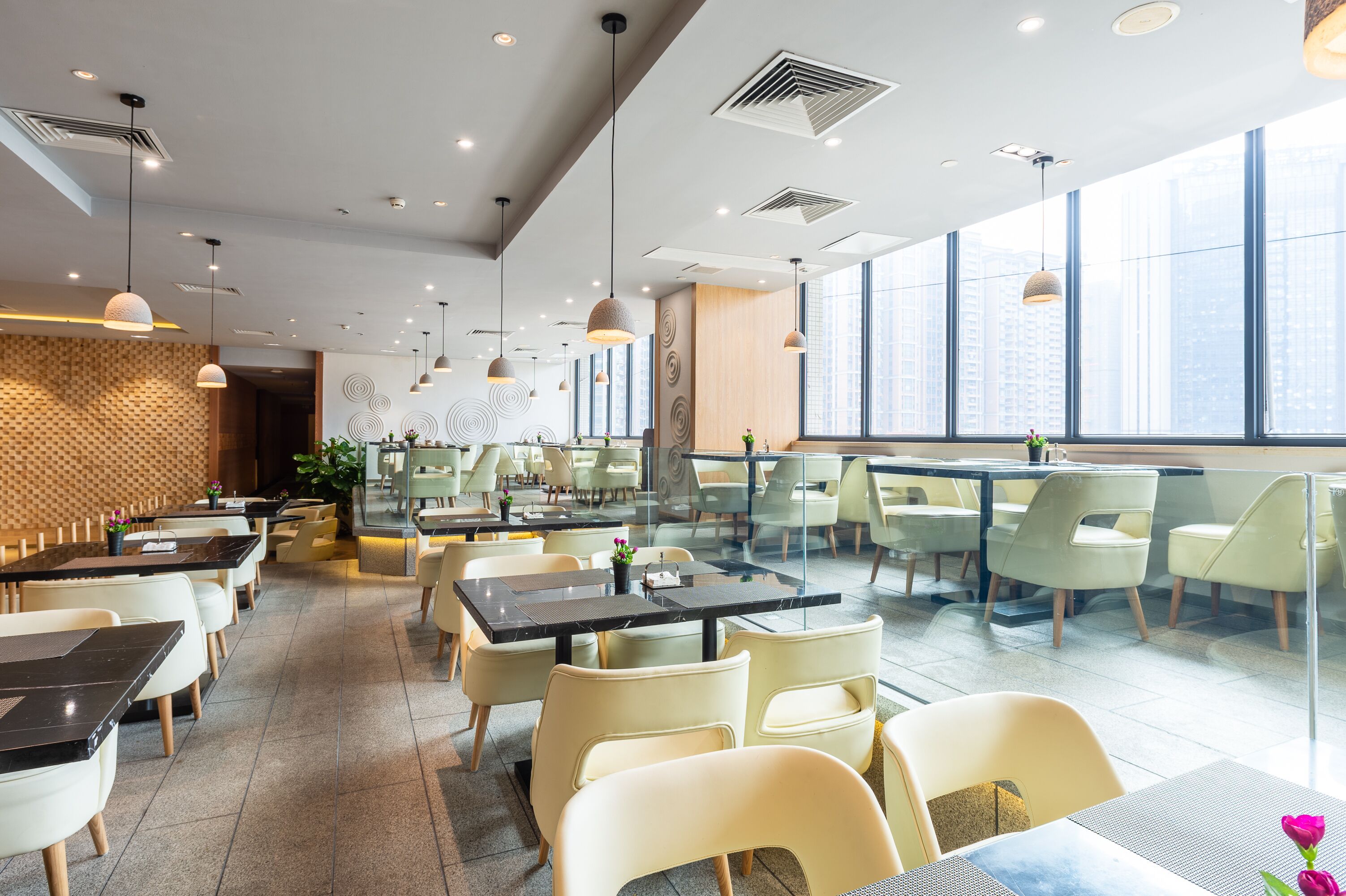 A modern restaurant with high ceilings, pendant lighting, and large windows offering views of the city.