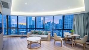 Una sala de estar moderna con una amplia vista de la ciudad, una mesa de centro redonda, un sofá con cojines y una pequeña mesa redonda con sillas.