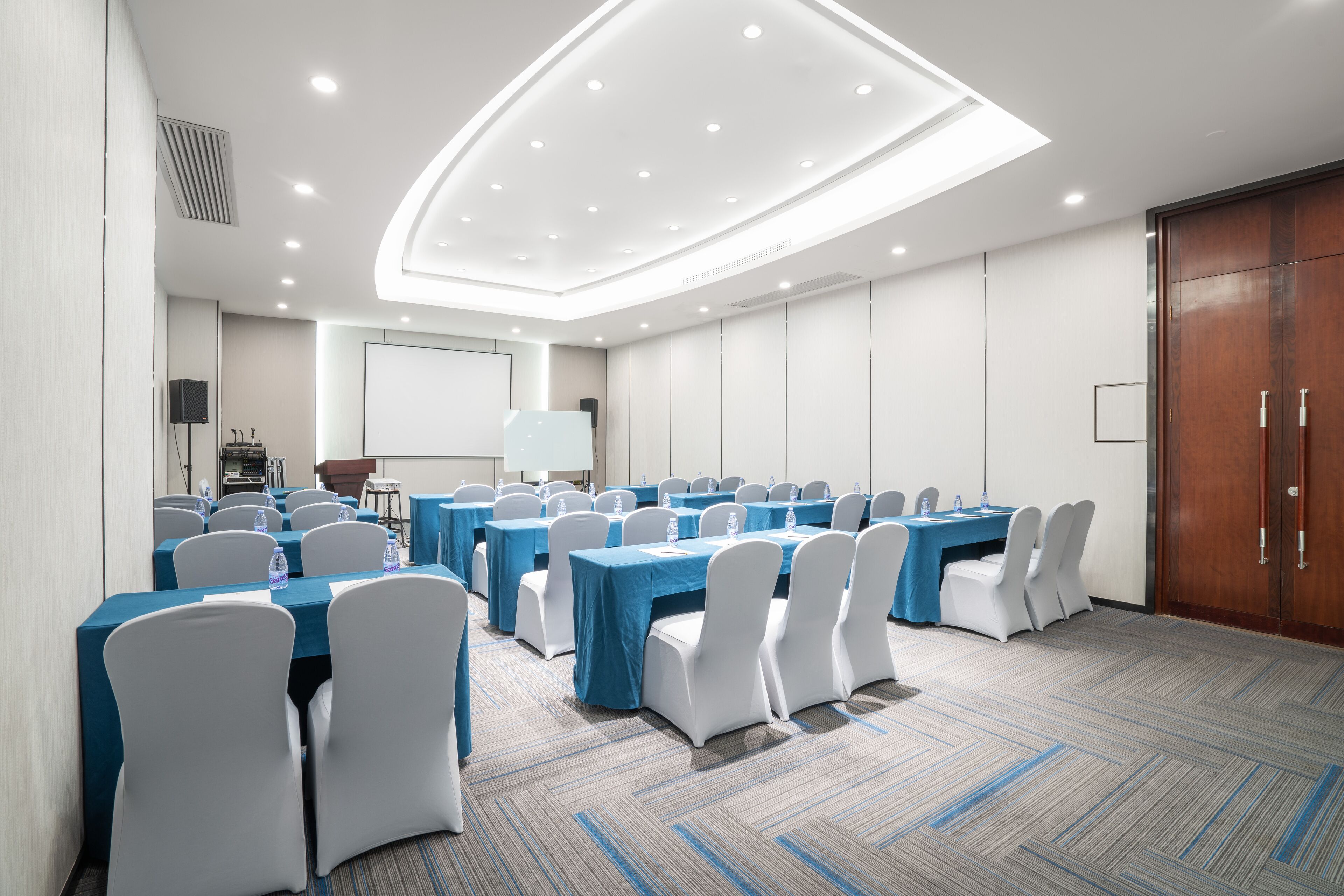 A conference room with multiple tables and chairs, a projector screen, and a wooden door.