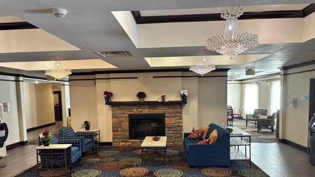 A hotel lobby with a stone fireplace, blue sofas, a patterned rug, and chandeliers.