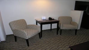 Two patterned armchairs, a small table with a telephone and papers, and a dark-colored cabinet against a plain wall.