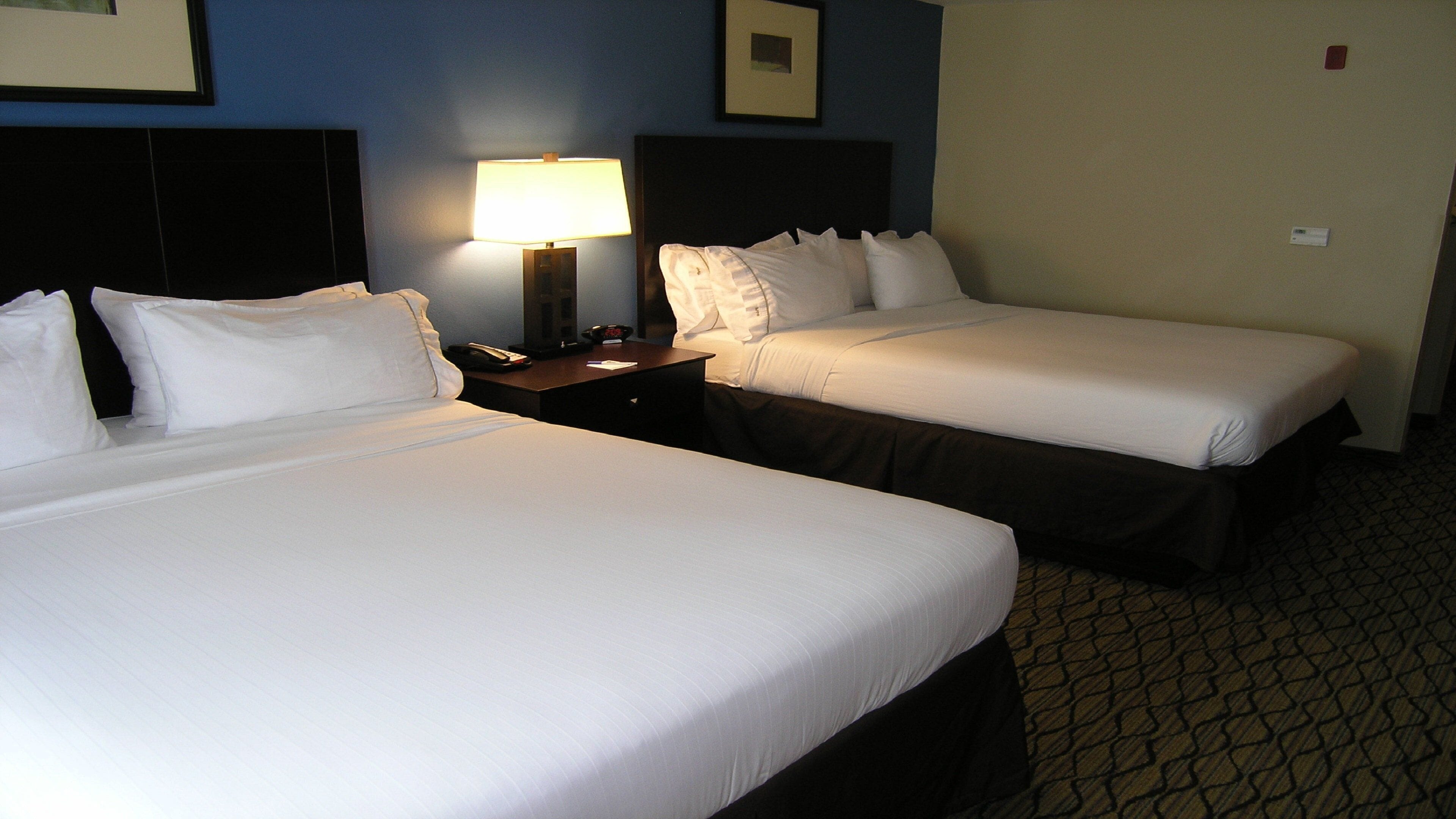 A hotel room with two beds, a nightstand with a lamp, and a framed picture on the wall.