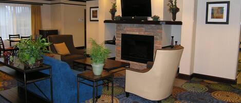 A hotel lobby with a fireplace, seating area, and a television.