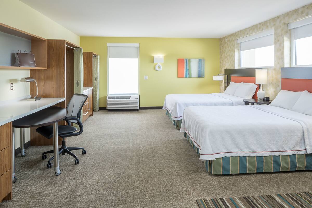 Een hotelkamer met een bureau, twee bedden, een stoel, een lamp en een raam.
