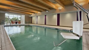 Een binnenzwembad met houten plafond, duikplank en uitzicht op buiten.