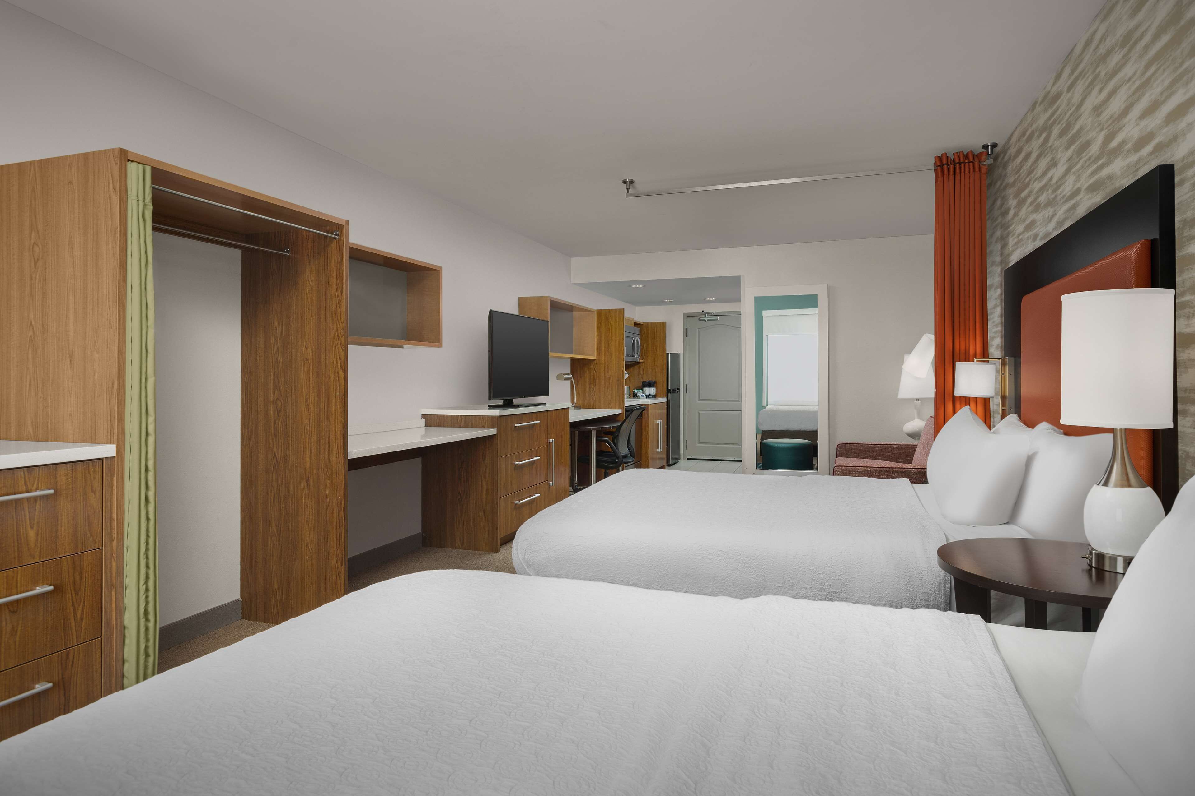 A hotel room with two beds, a desk, a television, and a bathroom visible through an open door.