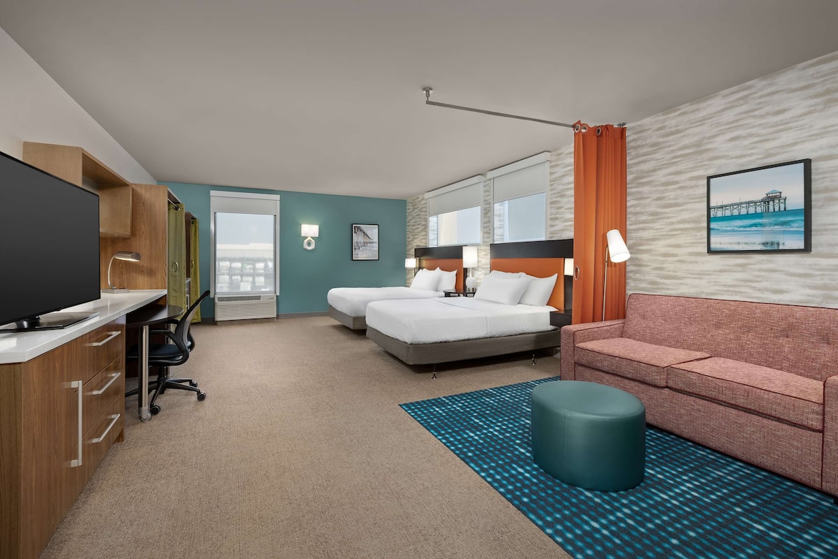 Een hotelkamer met een bed, een slaapbank, een bureau met een televisie, een bureaulamp en een raam met gordijnen.