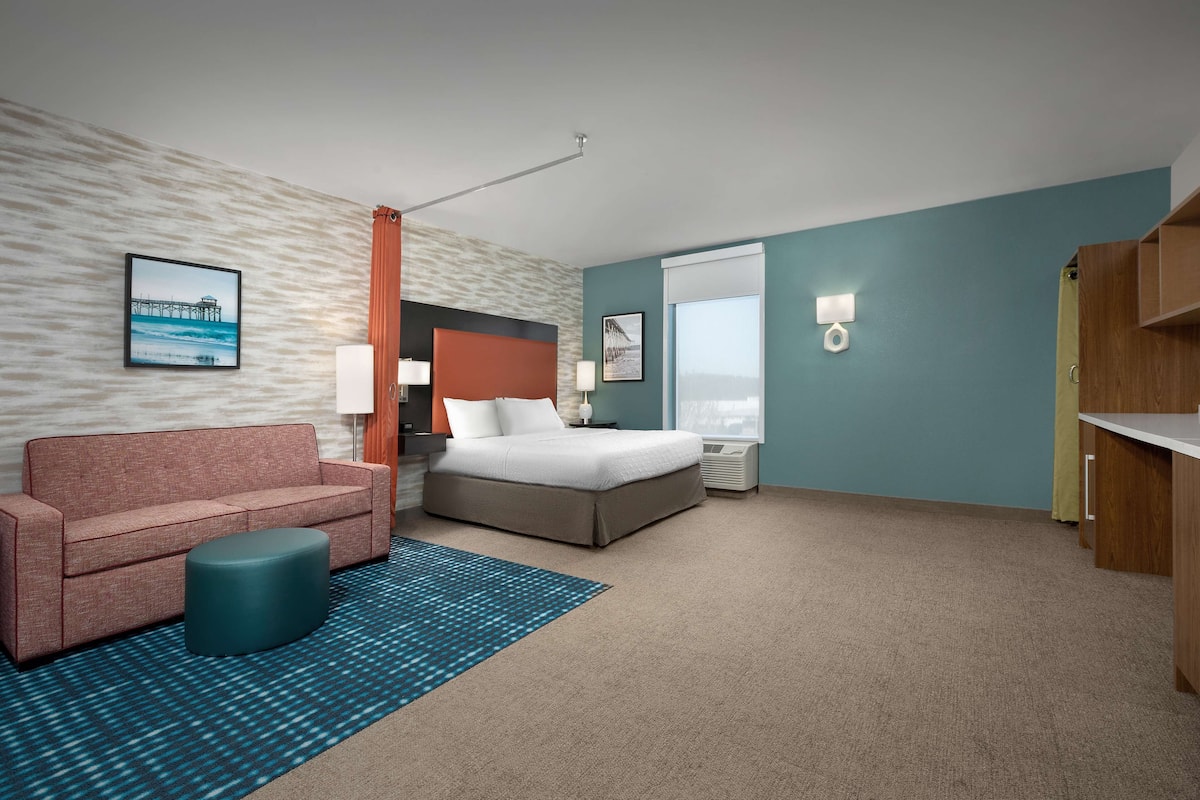 Een hotelkamer met een bed, een bank, een tafeltje, een nachtkastje en een raam met gordijnen.