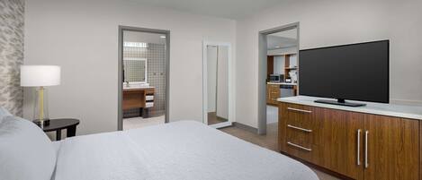 Quarto de hotel com uma cama grande, televisão, escrivaninha e banheiro visível por uma porta aberta.
