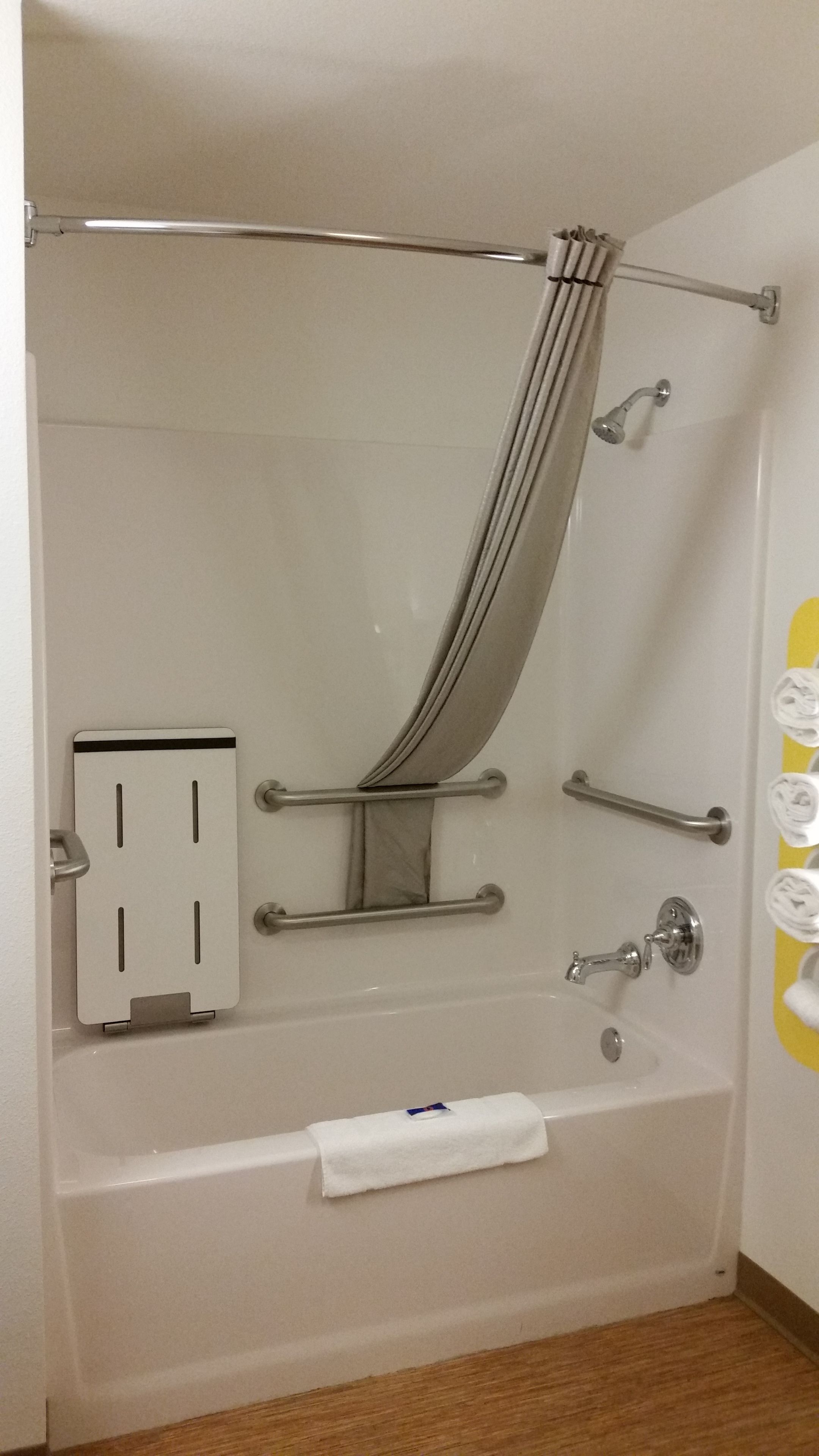 A modern bathroom with a walk-in shower, grab bars, a towel rack, and a toilet paper holder.