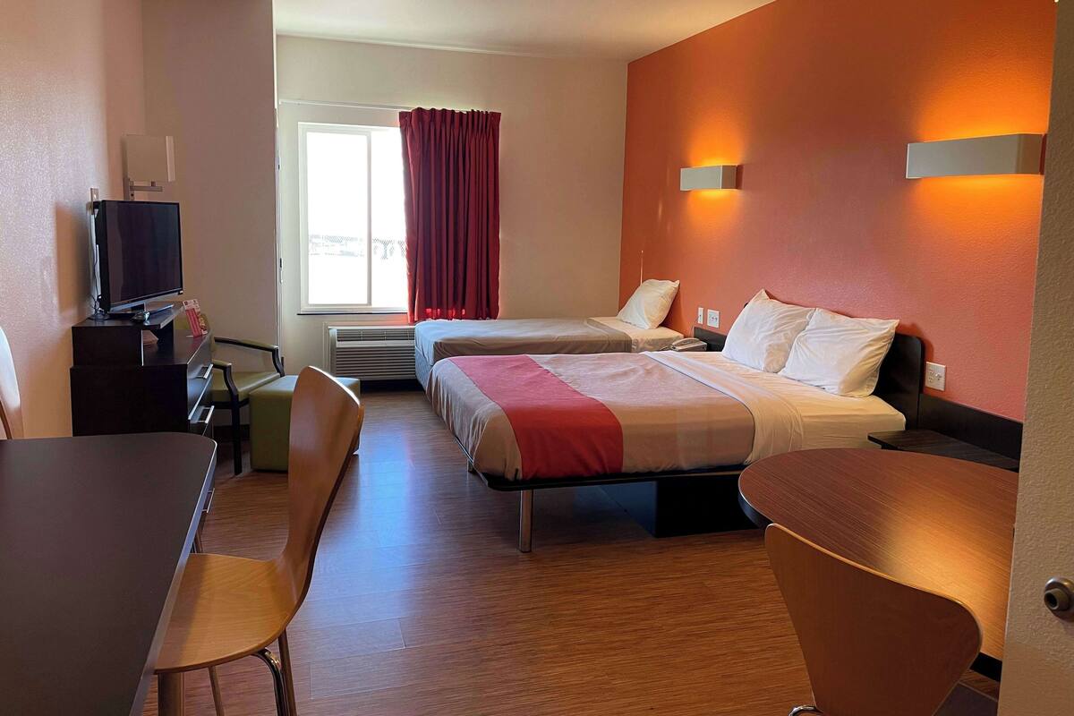 Habitación de hotel con dos camas, un escritorio, una silla, un televisor y una ventana con cortinas.