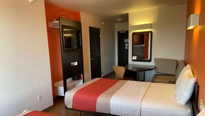 A hotel room with two beds, a desk, a chair, and a small table with a phone.