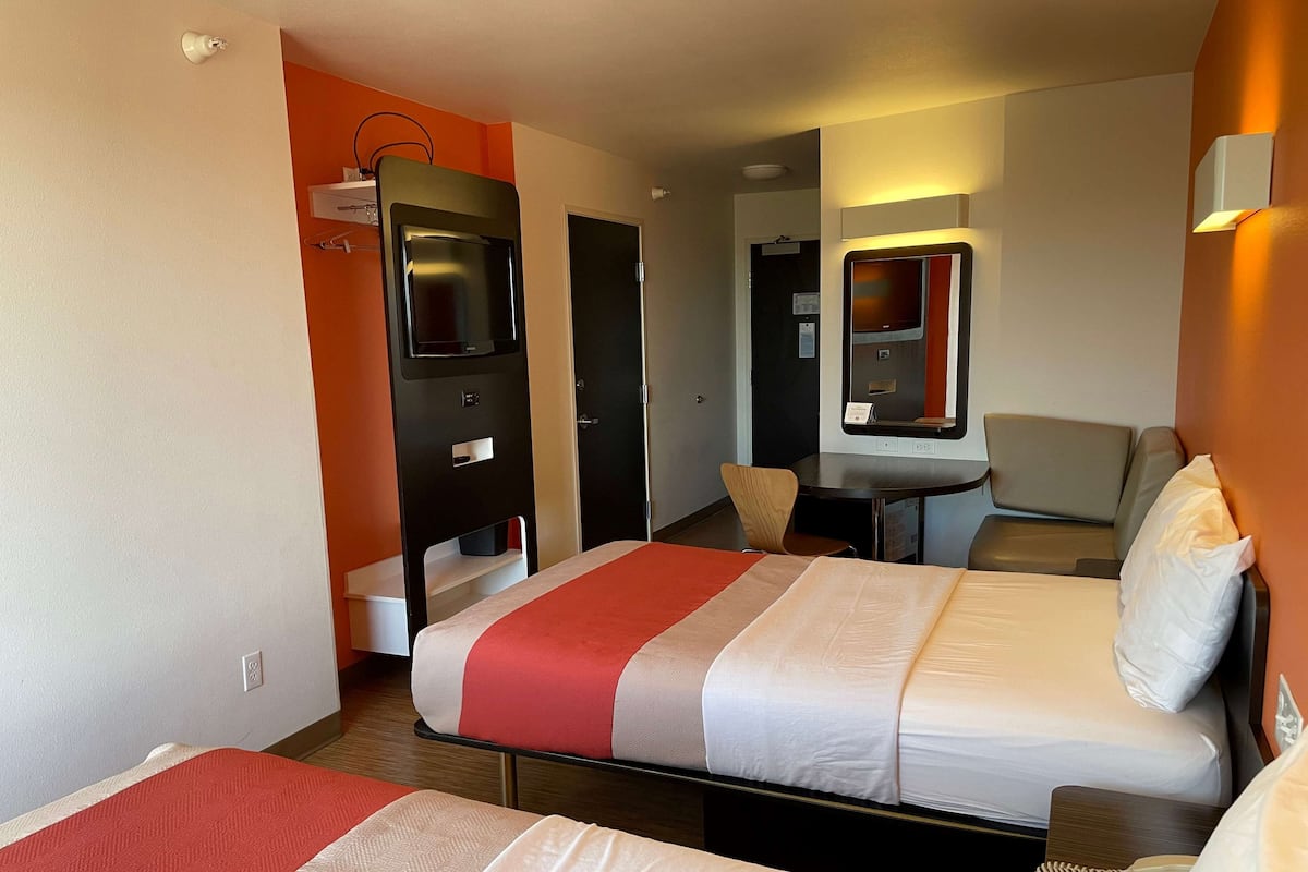 Una habitación de hotel con dos camas, un escritorio, una silla y una mesita con un teléfono.
