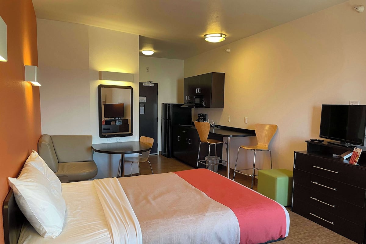 Una habitación de hotel con cama, escritorio, kitchenette y televisor.