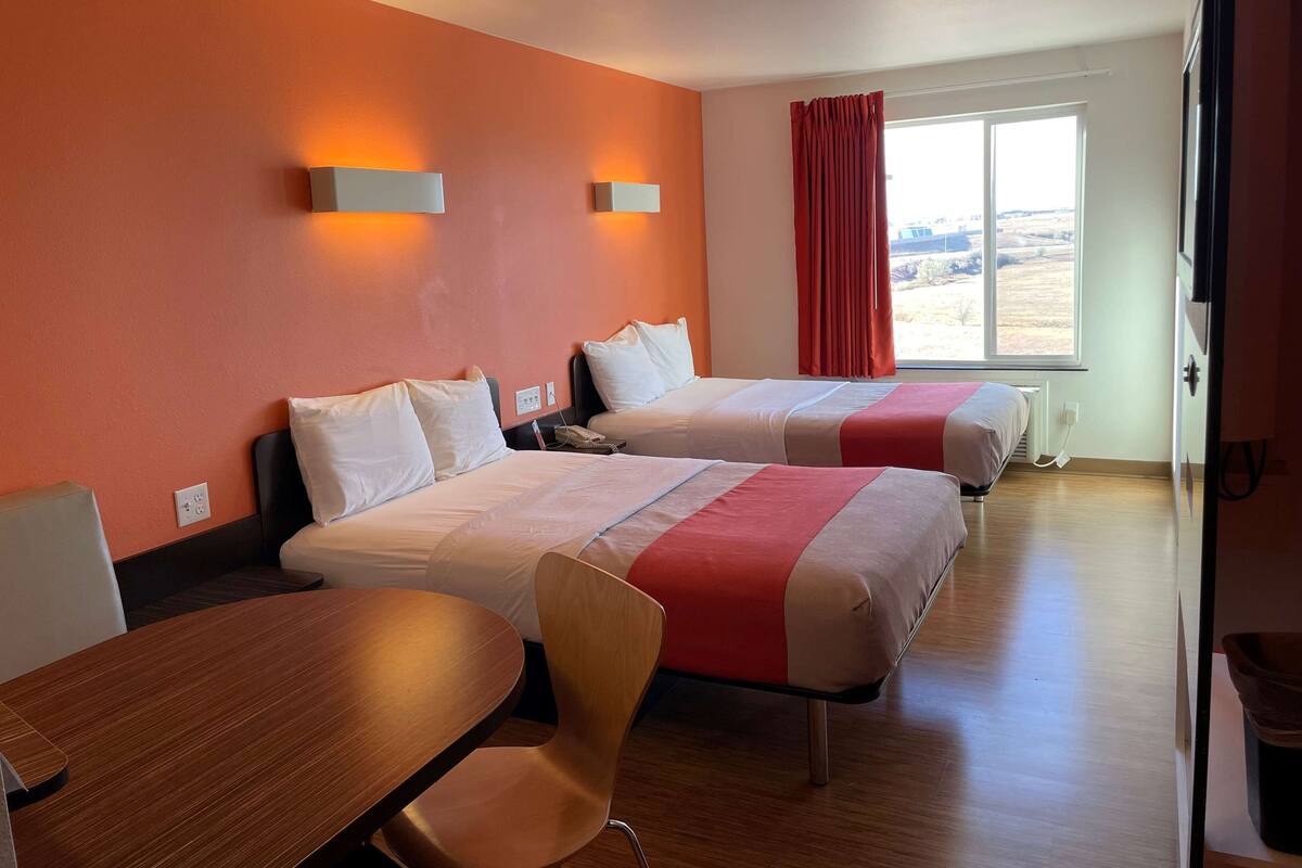 Habitación de hotel con dos camas, una mesa de madera y una silla.
