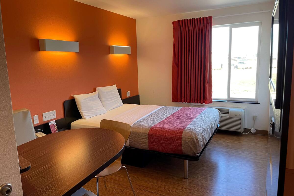 Una habitación de hotel con cama, escritorio y ventana con cortinas.