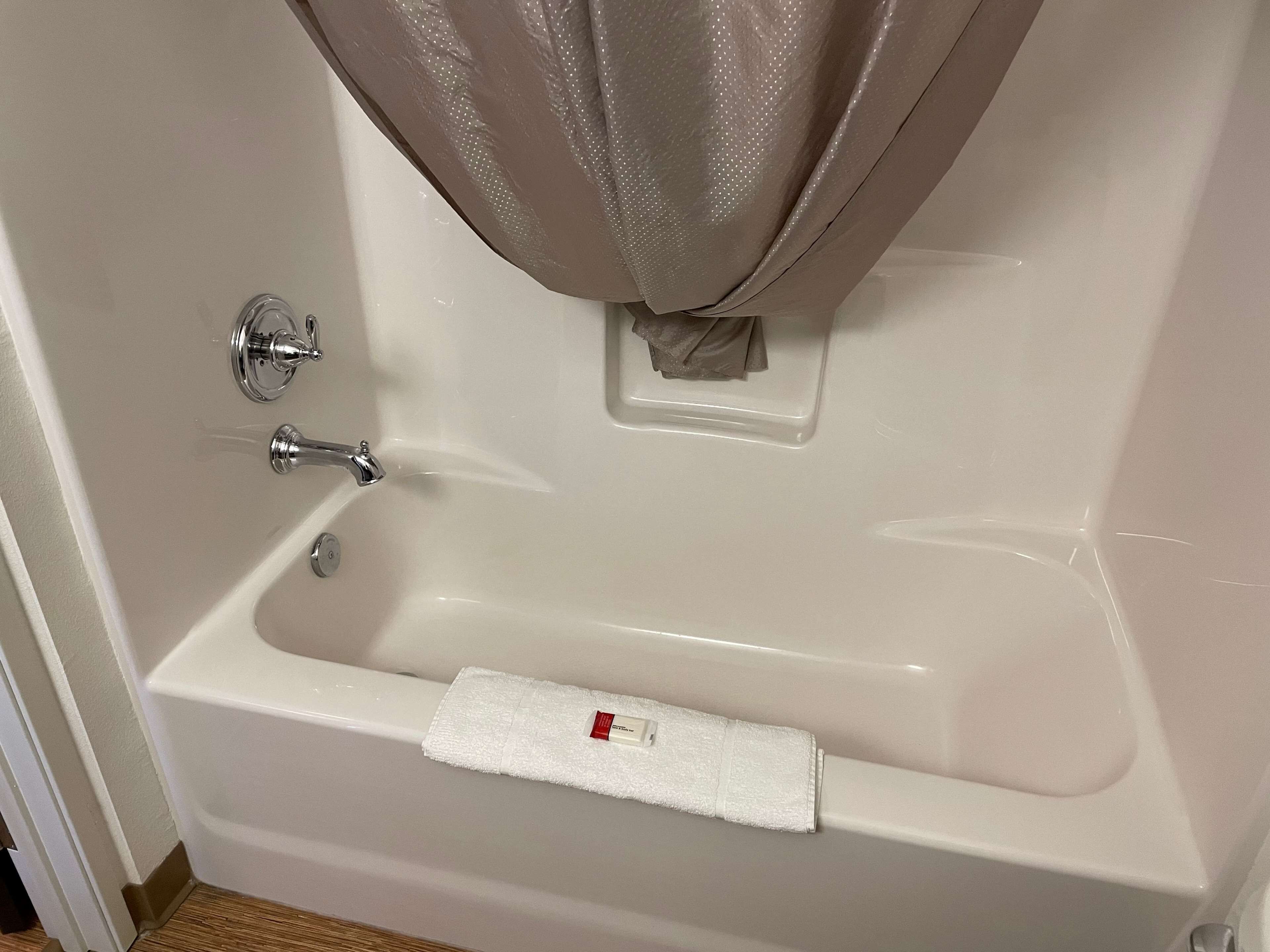 A white bathtub with a shower curtain, a towel, and a soap dispenser.