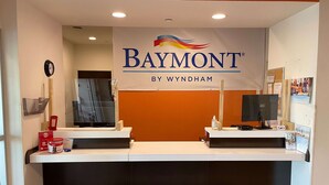 A reception area with a Baymont by Wyndham sign, two reception desks, a clock, a phone, and a small table with a bottle and tissues.