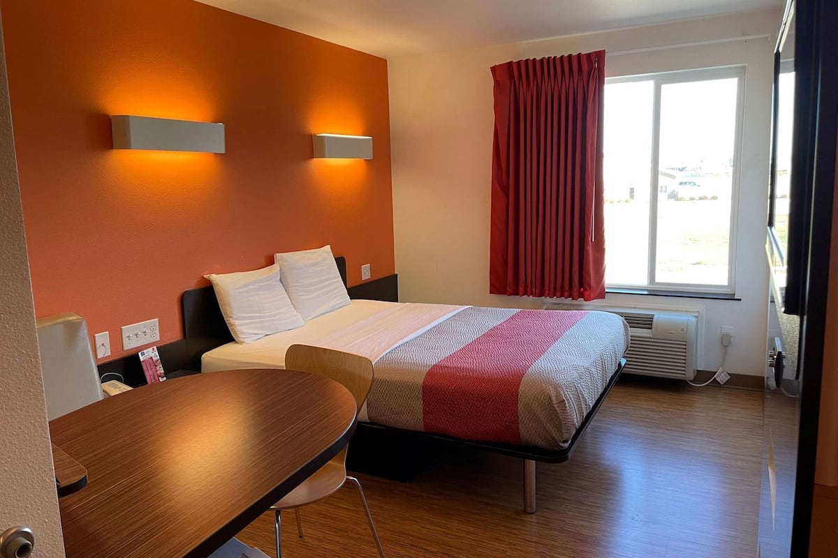 Una habitación de hotel con cama, escritorio, ventana con cortinas y un calentador de pared.