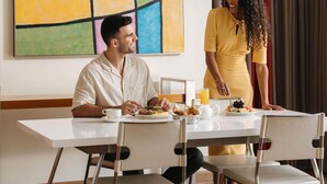 A dining area with a table set for two, a large abstract painting on the wall, and a red curtain in the background. - ibis Abu Dhabi Gate (Abu Dhabi)