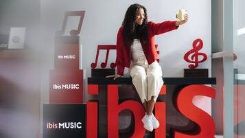 Une personne est assise sur une plateforme. De grandes lettres rouges forment le mot « IBIS MUSIC », et des notes de musique sont visibles en arrière-plan.