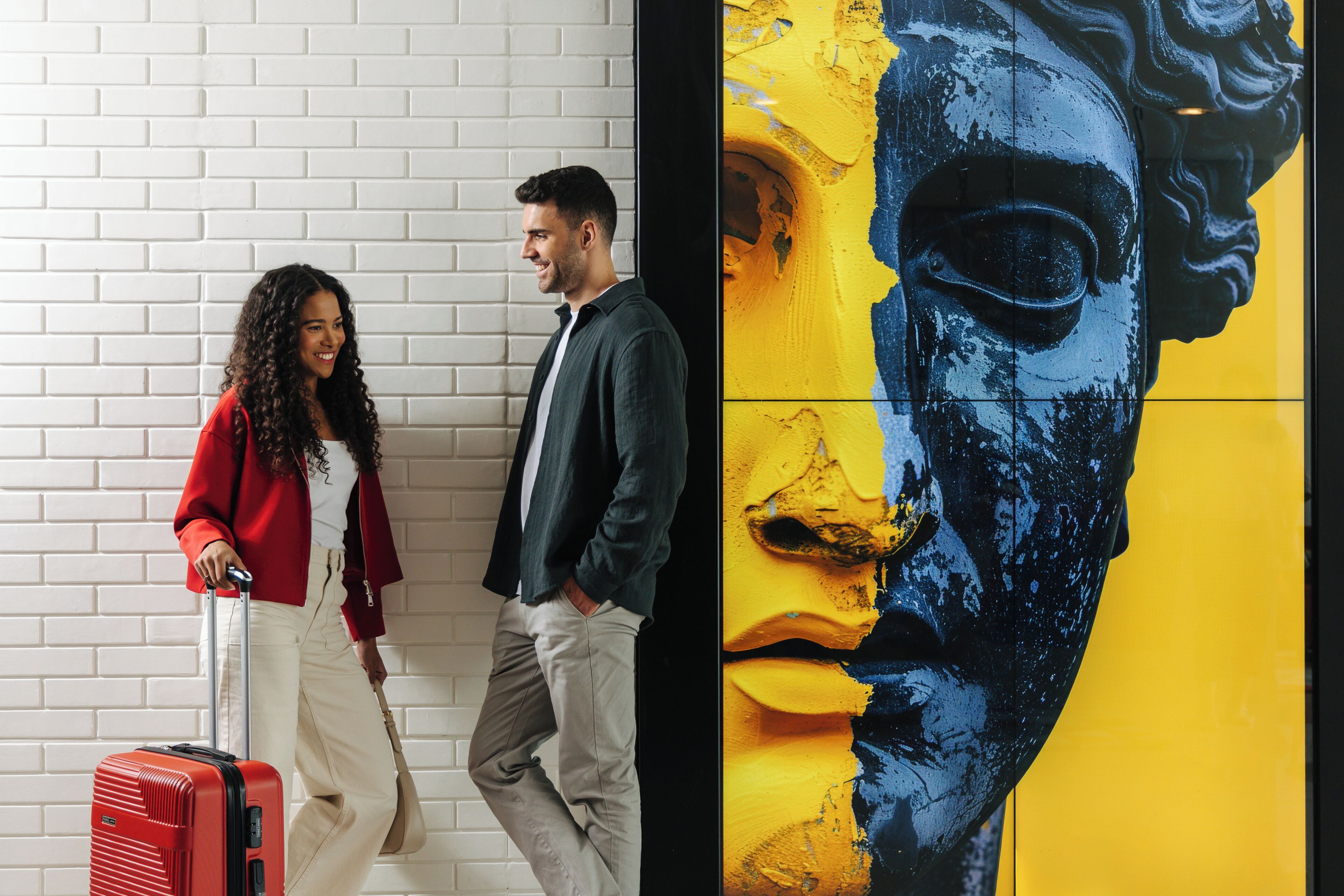 A man and a woman walking past a wall with a large, colorful mural.