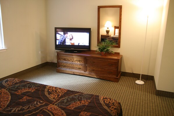 Habitación de hotel con una cama, un televisor sobre una cómoda de madera, un espejo y una lámpara de pie.