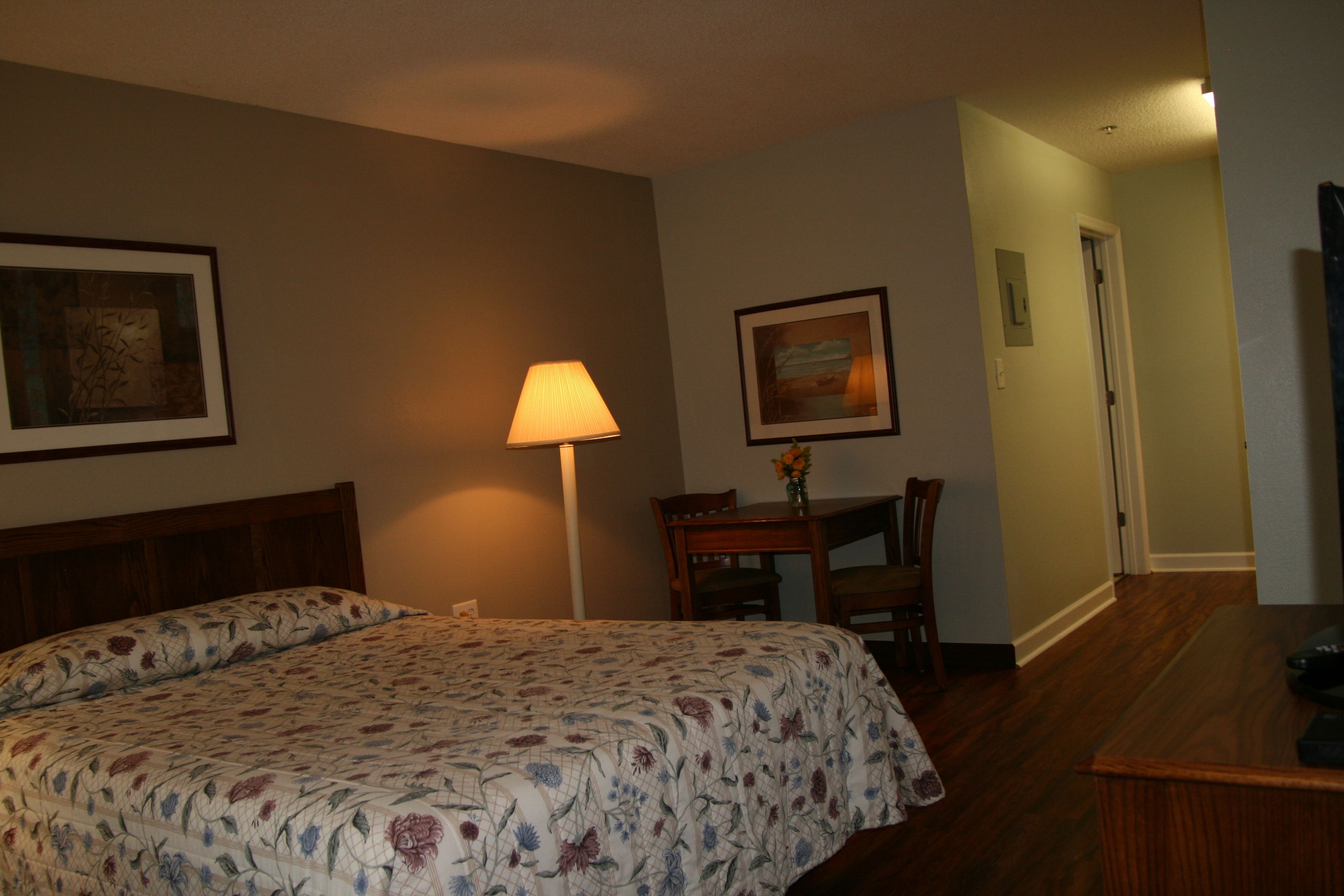 A hotel room with a bed, a desk, a chair, a lamp, and two framed pictures on the wall.