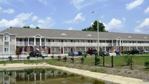 Ein Motel mit einer Reihe von Zimmern, einem Parkplatz und einem kleinen Teich.