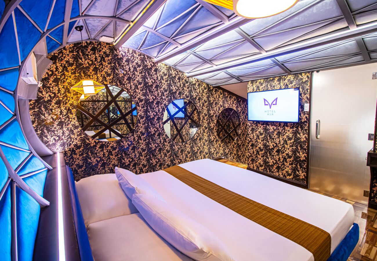 Una habitación de hotel moderna con cama, televisión y un diseño de techo geométrico único.