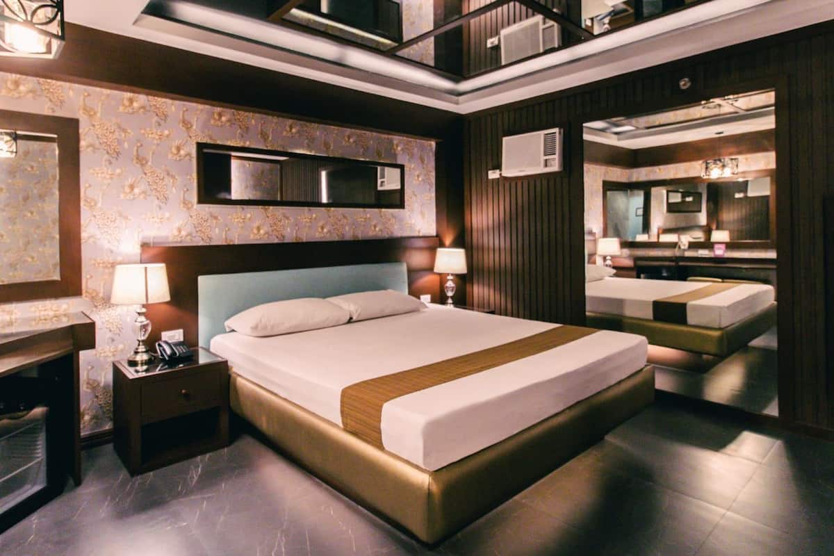 A modern hotel room with a large bed, a bedside table, a lamp, a mirror, and a wardrobe.