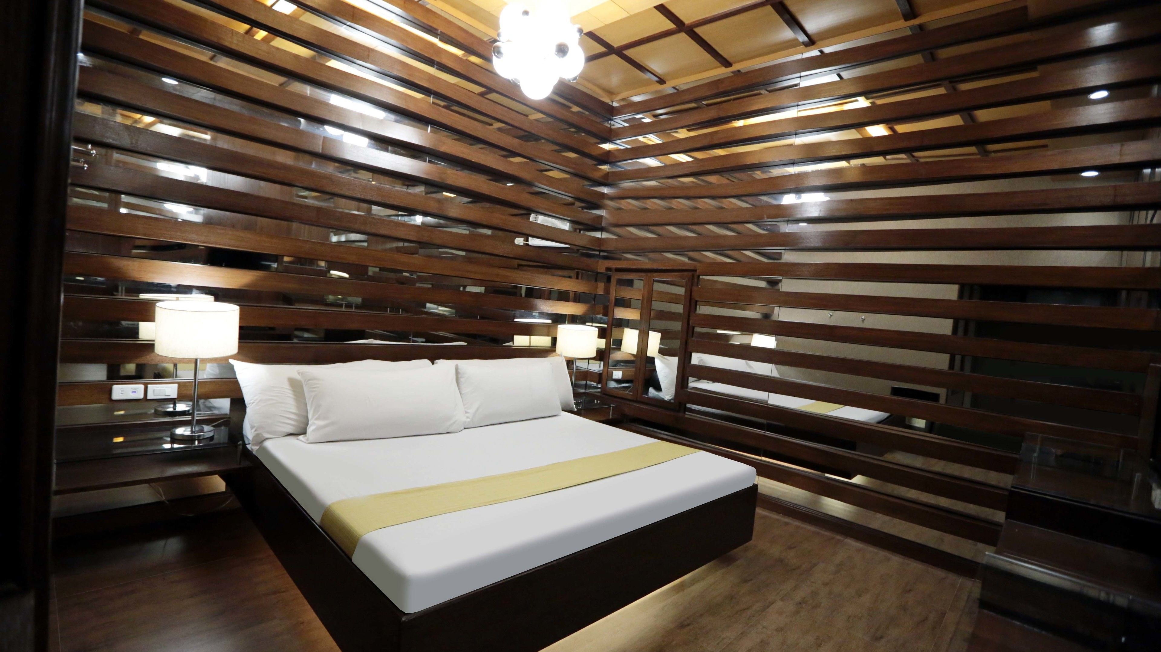 A modern hotel room with a wooden slat ceiling, a large bed with white linens, two bedside lamps, and a mirror on the wall.