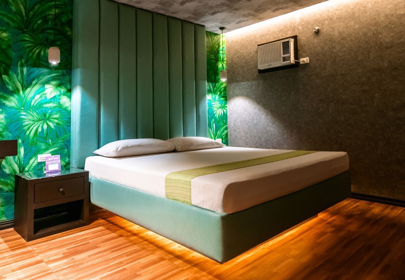 Une chambre moderne avec un lit, une table de chevet et un mur recouvert d’un papier peint aux motifs tropicaux.